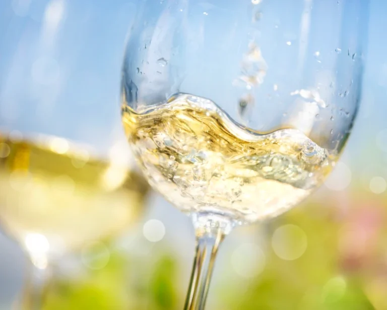 Nærbillede af hvidvin, der bliver skænket i et glas med sollys og sløret baggrund.